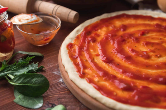 Low-Carb Pizza Sauce spread evenly on a pizza base with herbs aroudn