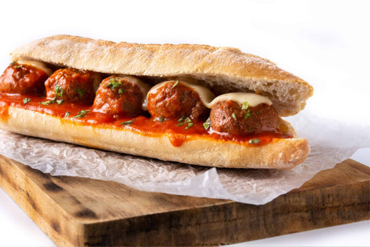a low-carb mozzarella and meatball sub sandwich on a wooden chopping board with a white background