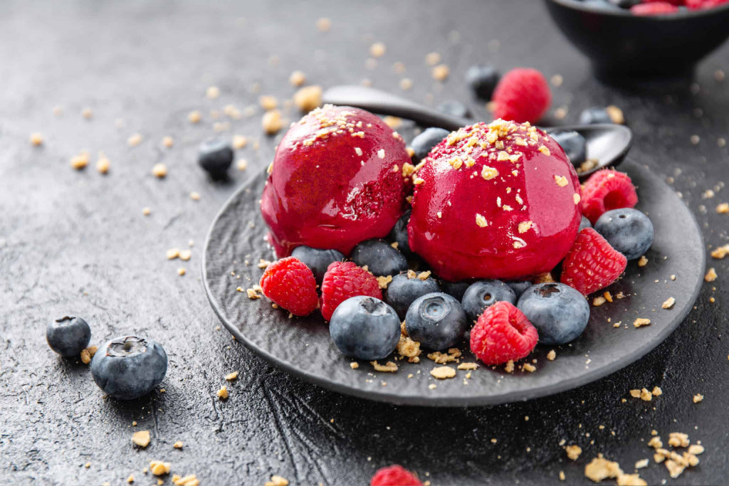 two scoops of low-carb berry sorbet on a bed of blueberries and raspberries