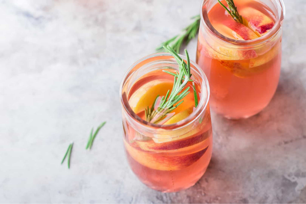 Low-carb peach gin and tea cocktail in a balloon glass with ice and peach slices.