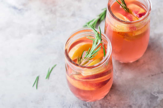 Low-carb peach gin and tea cocktail in a balloon glass with ice and peach slices.