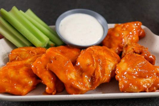 5 creamy buffalo chicken thighs on a white plate, with a sour creme dip and celery