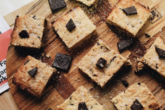 8 squares of low-carb choclate blondies arranged on a wooden chopping board, each with a square of chocolate on top. 