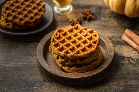Low-carb pumpkin waffles stacked on a plate with butter melting on top.