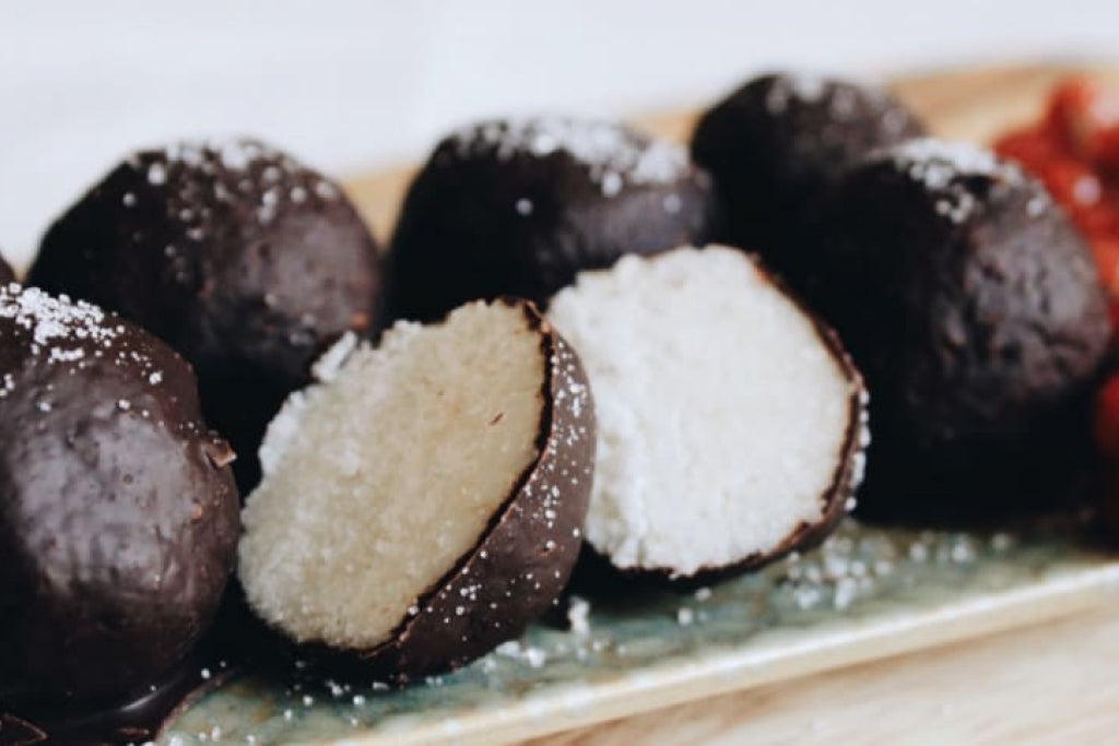 Low-carb coco bites coated in chocolate arranged on a slate board.