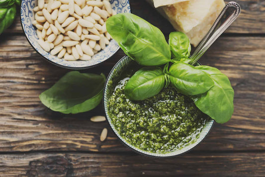 Low-carb green pesto in a glass jar with fresh basil leaves alongside.