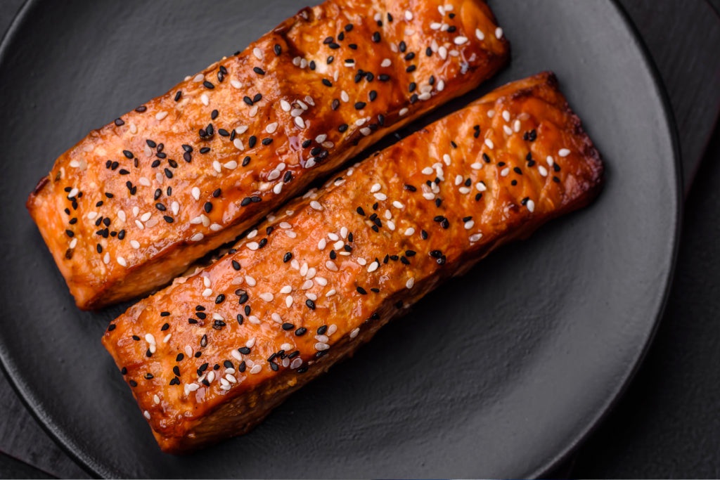 Sesame crusted salmon fillets with black and white seeds on a dark serving plate.