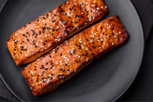 Sesame crusted salmon fillets with black and white seeds on a dark serving plate.
