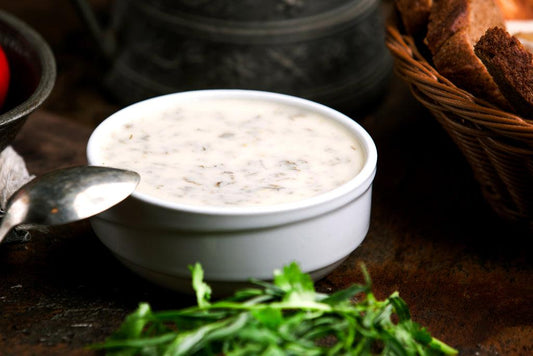 a close up photo of a white bowl with home made low-carb ranch dressing. A silver spoon is resting on the edge of the bowl