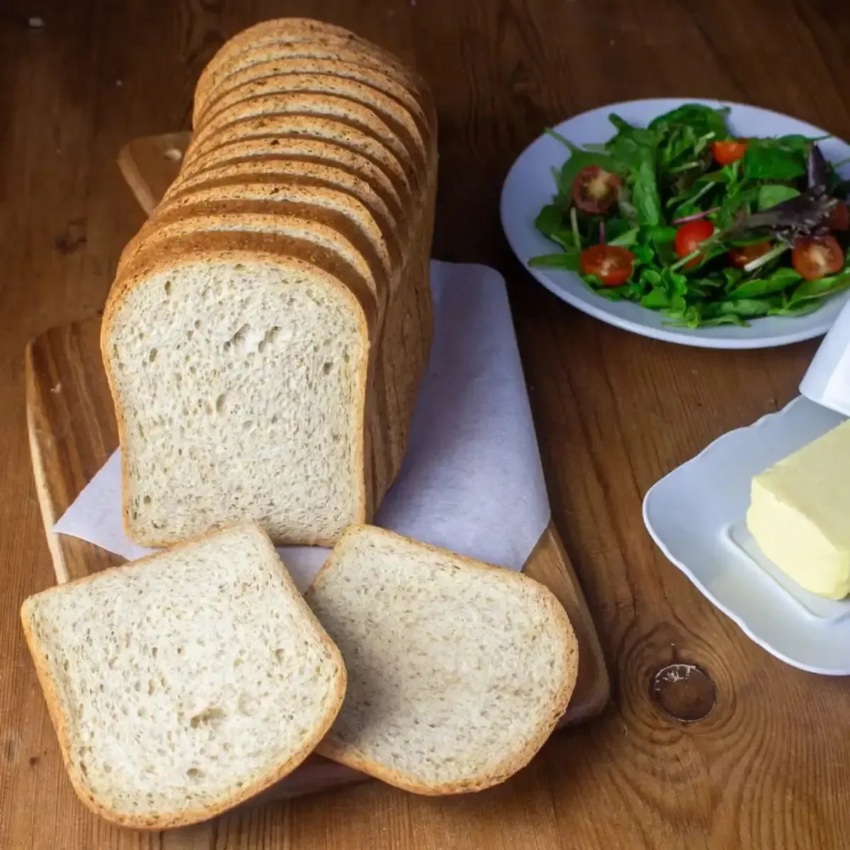 Freshly sliced 700g loaf of white bread on a wooden board with butter and a side salad.