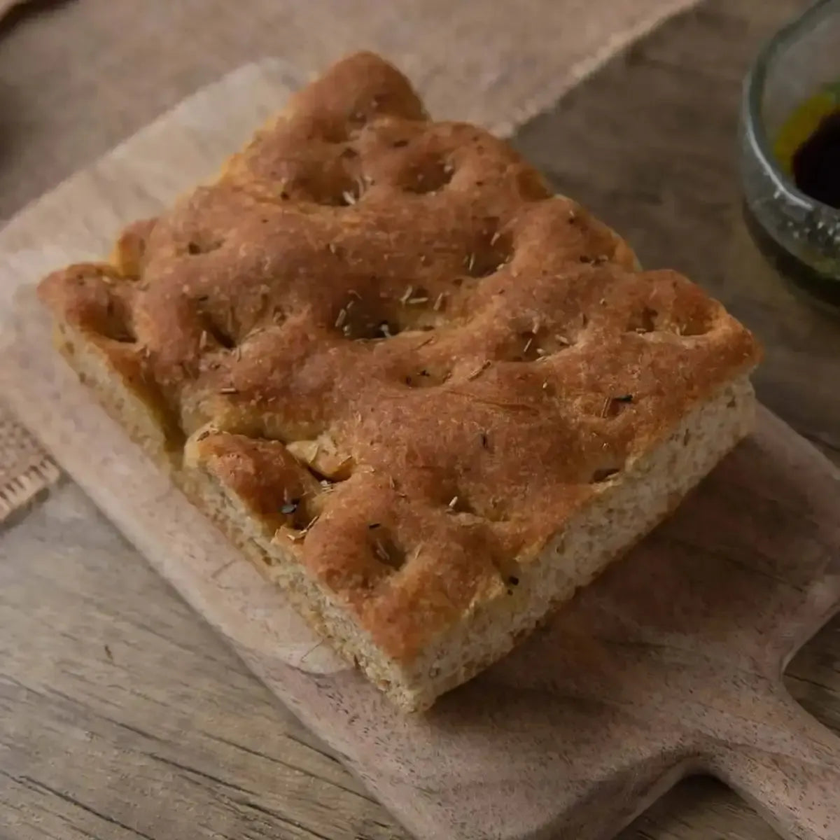 Golden focaccia bread with rosemary on a rustic wooden board, ready for dipping.