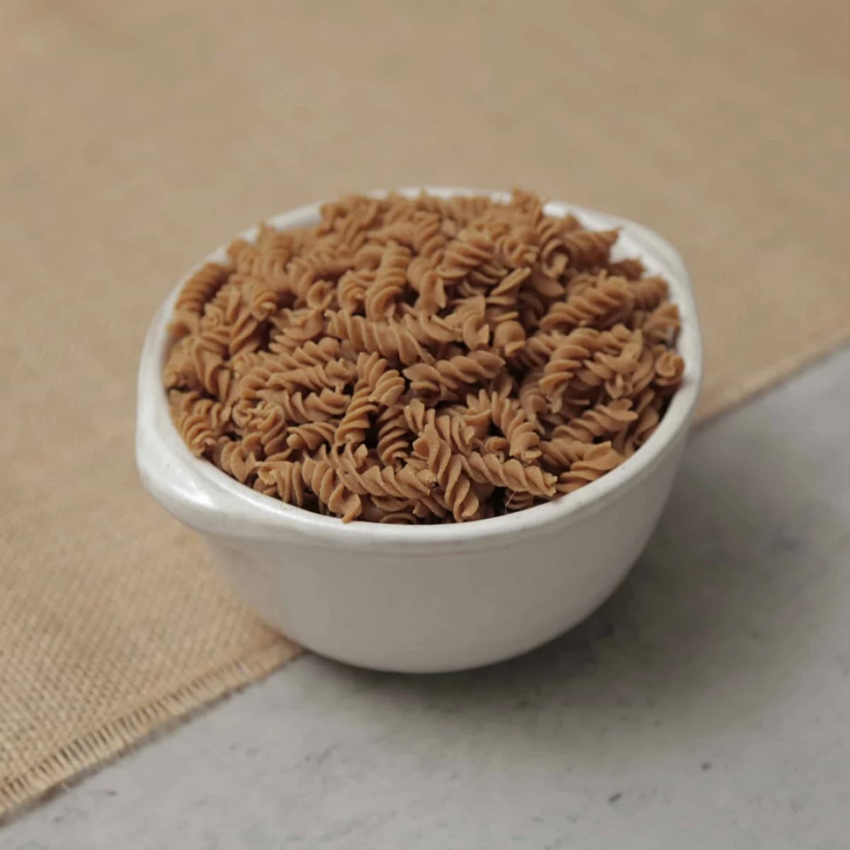 Bowl of low-carb fusilli pasta on a rustic burlap surface.