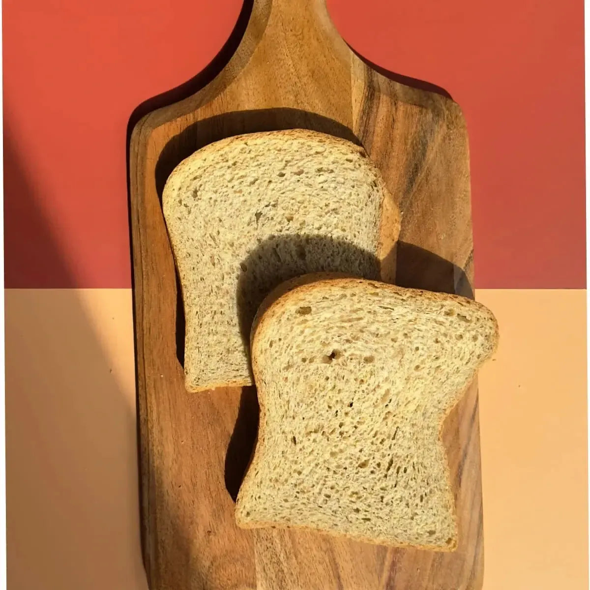 Two slices of whole wheat bread on a rustic wooden cutting board, against a warm two-toned background.