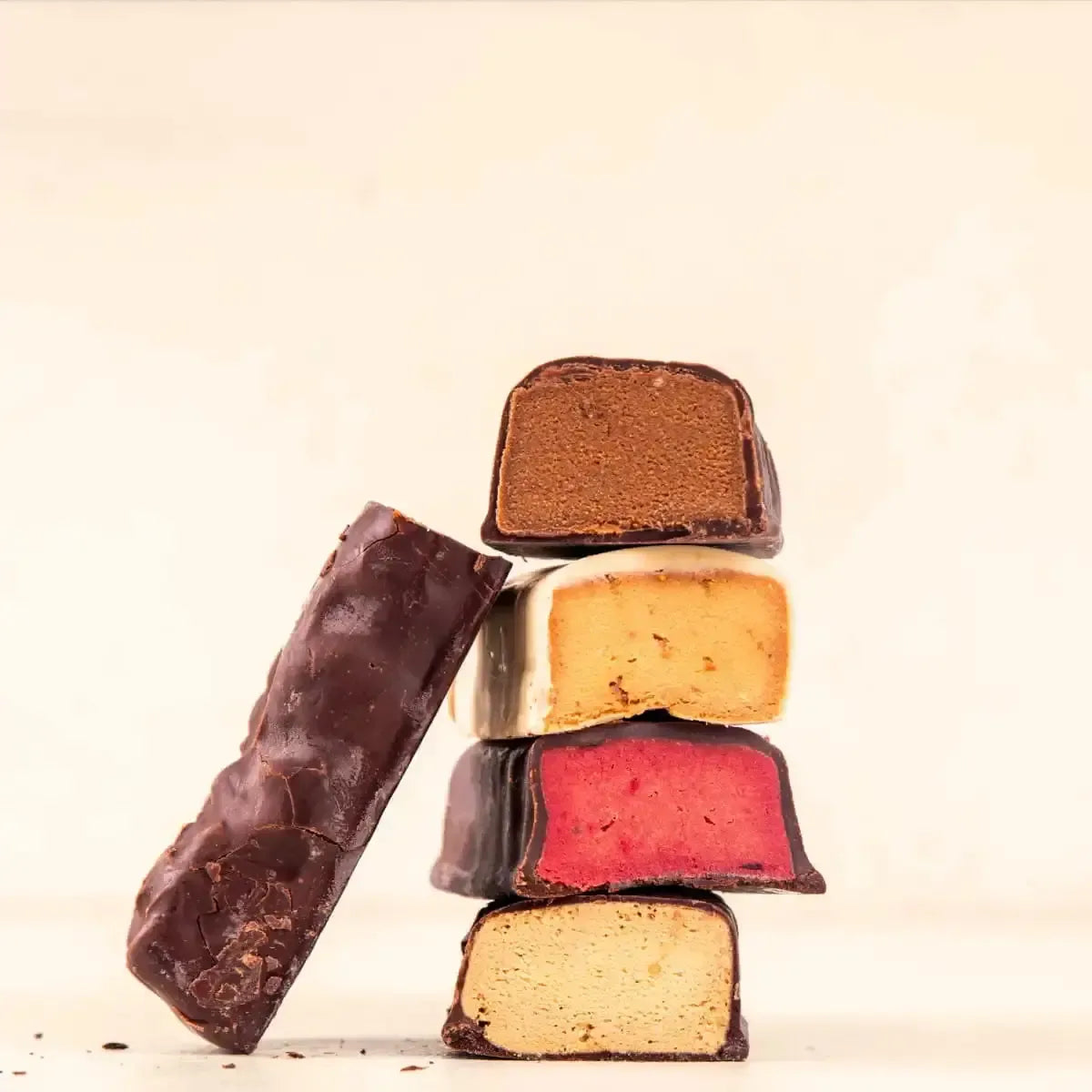 Stacked chocolate-covered snack bars with colorful fillings: brown, cream, red, and tan.