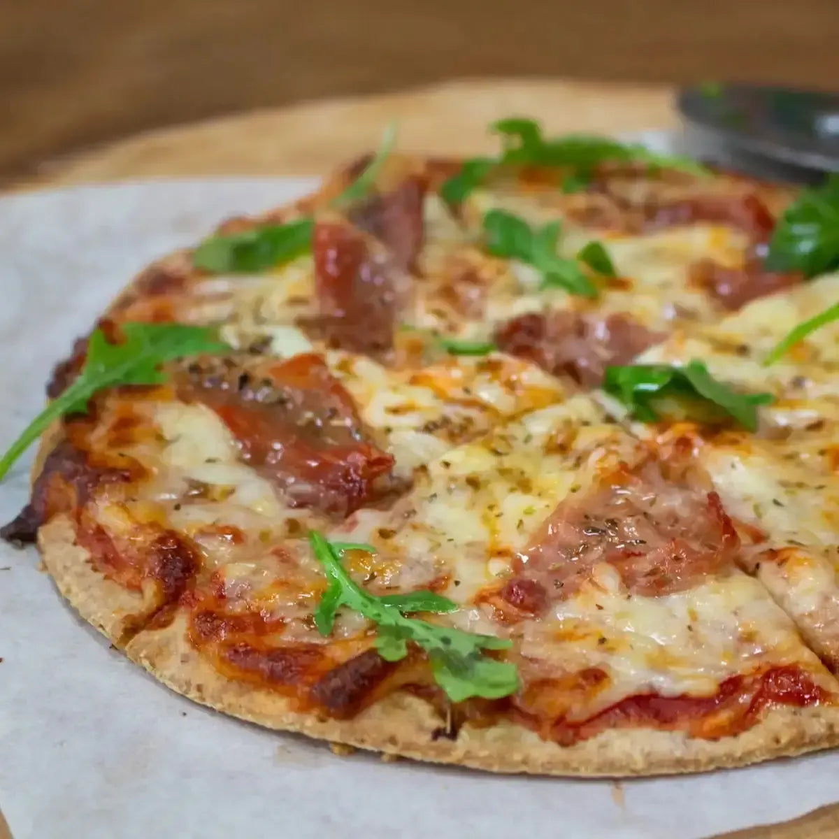 Warm, cheesy pizza with prosciutto and fresh arugula on a rustic wooden board.
