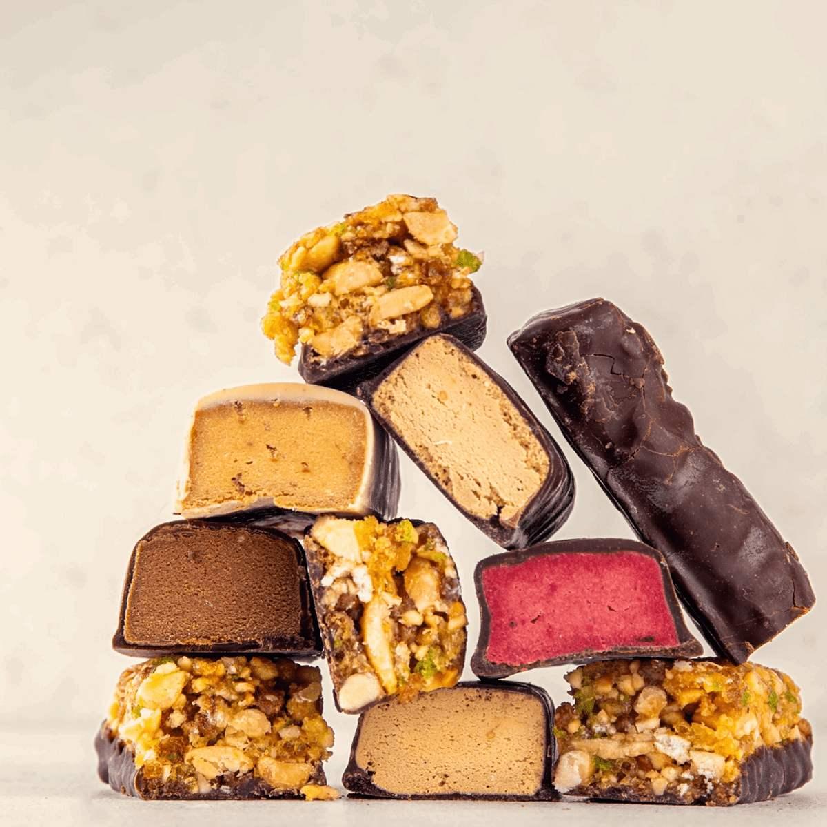 A vibrant stack of assorted snack bars and candies, featuring chocolate, nougat, and fruit fillings.