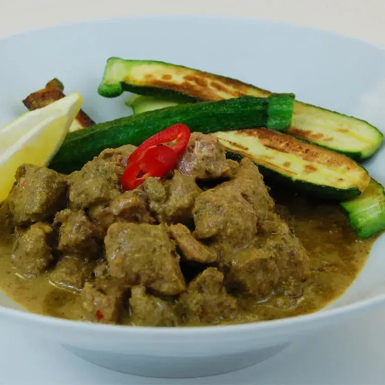 Keto Sri Lankan Beef Curry with creamy sauce, red chili, lemon wedge, and grilled zucchini in a white bowl.