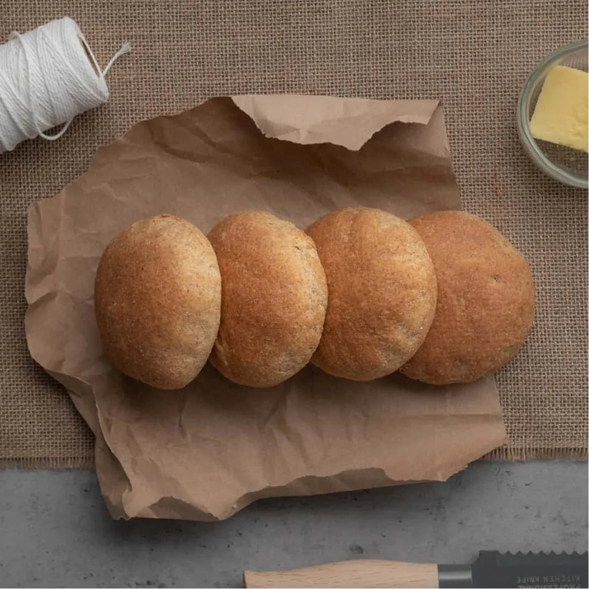 Four golden-brown keto bread rolls on crumpled brown paper, with string and butter.