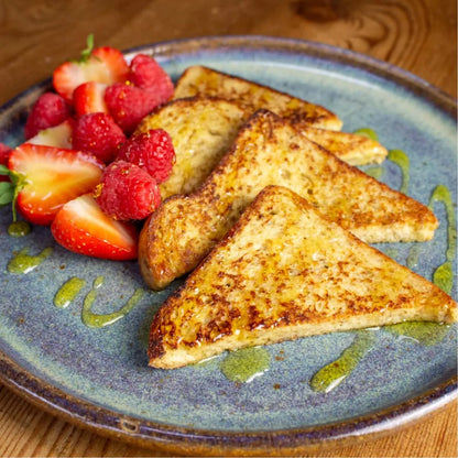 Golden keto French toast slices with fresh strawberries, raspberries, and green drizzle on a blue plate.