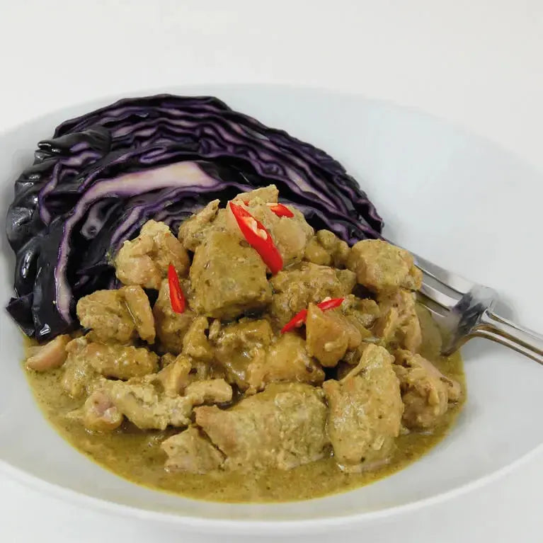 Keto Green Thai Chicken Curry with red cabbage, garnished with red chili slices, in a white bowl.