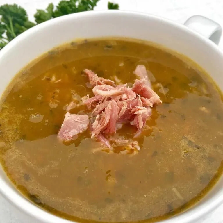 Rich, golden ham hock broth with shredded ham, served in a white ceramic bowl.