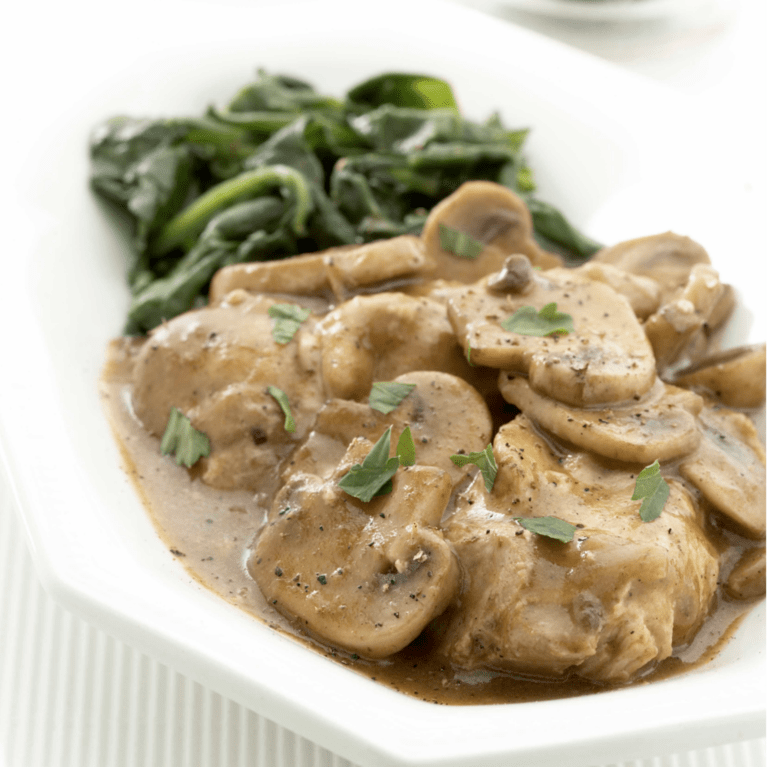 Keto Coq Au Vin with chicken, sliced mushrooms, rich brown sauce, and green spinach on a white plate.
