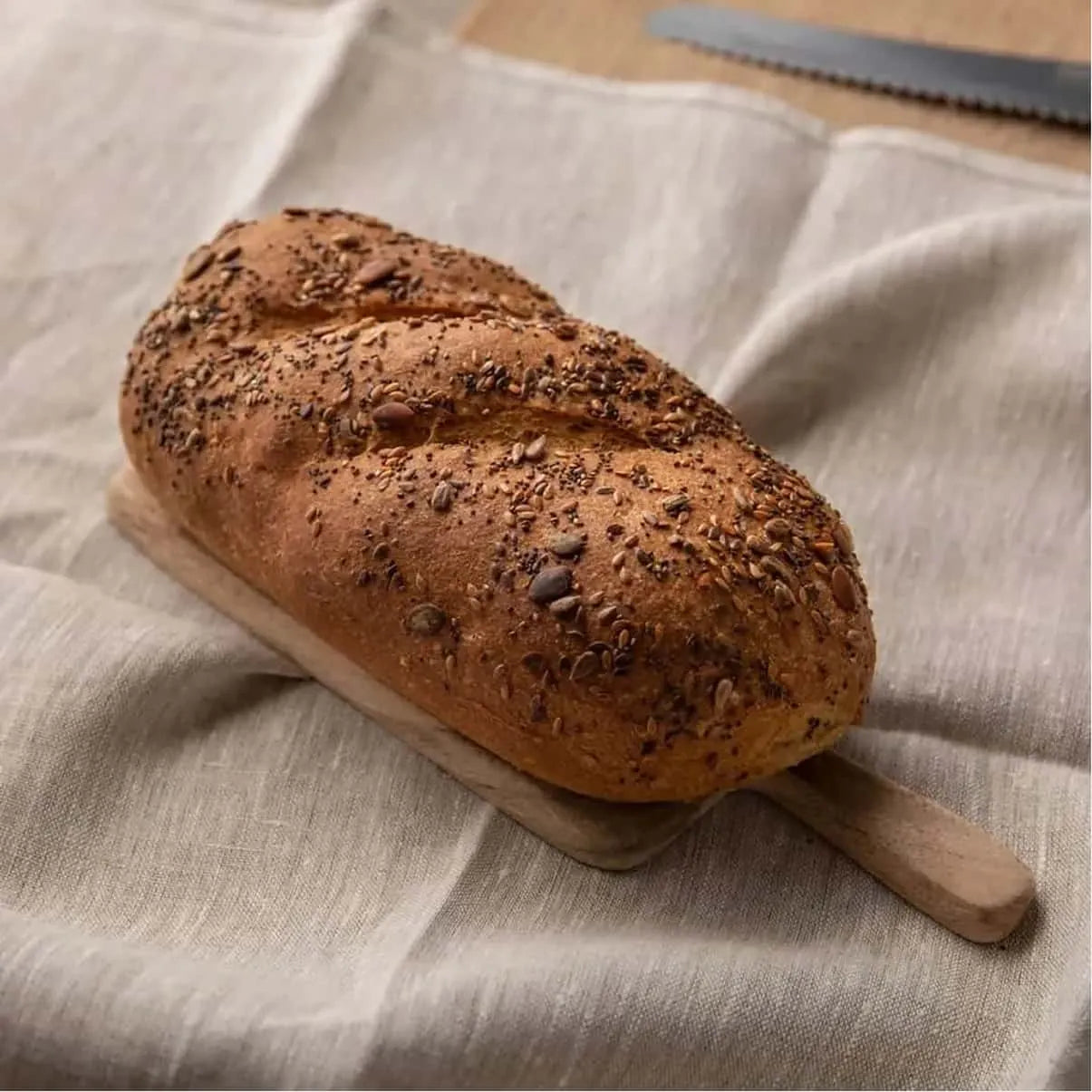 Golden brown seeded low-carb bloomer bread on a small wooden board, resting on a beige linen cloth.
