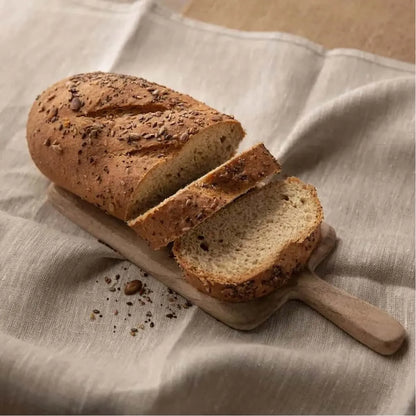 Sliced low-carb seeded bloomer bread on a wooden board, resting on a beige linen cloth.