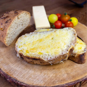 Toasted low-carb seeded bloomer bread with melted cheese, a loaf slice, cheese block, and cherry tomatoes on wood.