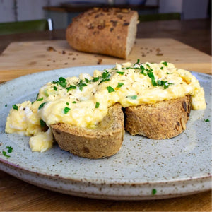 Two slices of seeded low-carb bloomer bread topped with scrambled eggs and parsley on a speckled plate.
