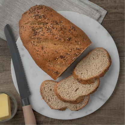 Seeded low-carb bloomer bread, partially sliced, on a white marble board with a bread knife and butter.