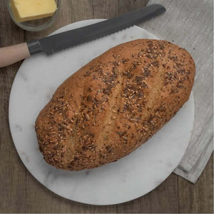 Golden brown seeded bloomer bread on a white marble board with a bread knife and butter.