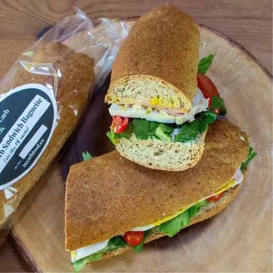 Two keto baguettes on a wooden board; one whole in packaging, one sliced with sandwich fillings.