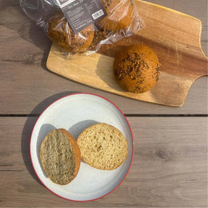Packaged and sliced keto seeded bread rolls on a wooden board and white plate.
