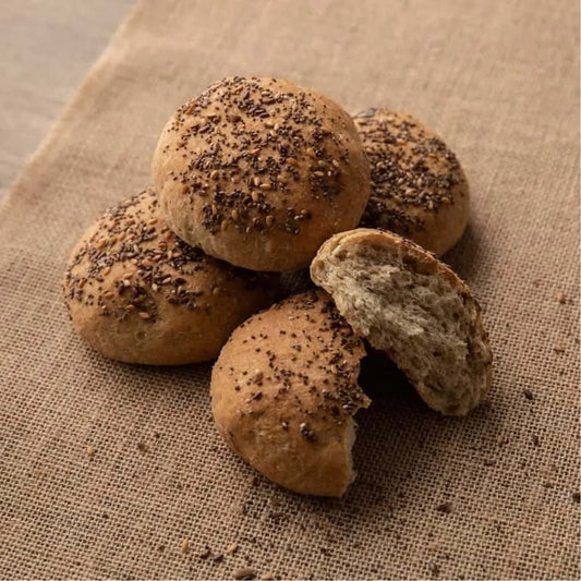 Four artisan keto seeded bread rolls on burlap, one broken open to show soft interior.