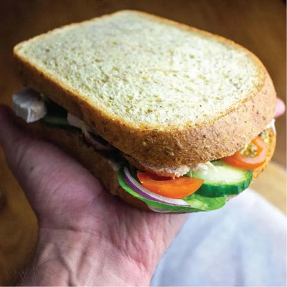 Hand holding a thick-sliced, light brown low-carb keto bread sandwich filled with fresh vegetables.