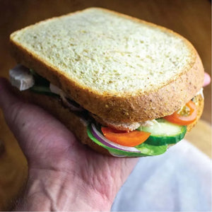Hand holding a thick-sliced, light brown low-carb keto bread sandwich filled with fresh vegetables.