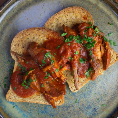 Two slices of toasted keto bread topped with rich red sauce and shredded meat, garnished with parsley.