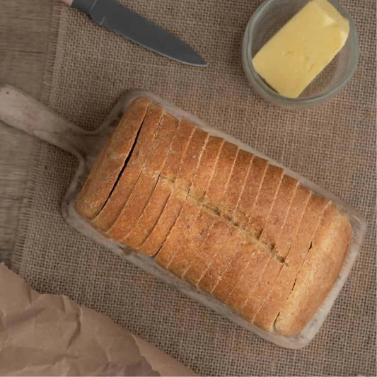 Sliced keto-friendly plain bread loaf on a wooden board with butter and a knife.