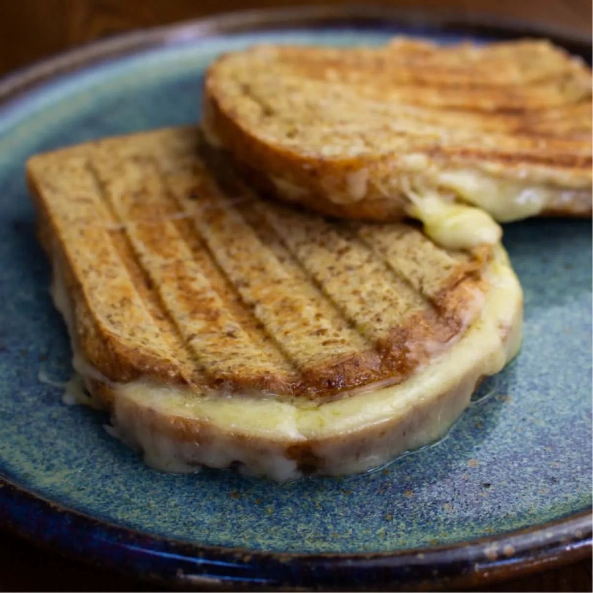 Two golden-brown grilled keto cheese sandwiches with melted filling on a blue ceramic plate.