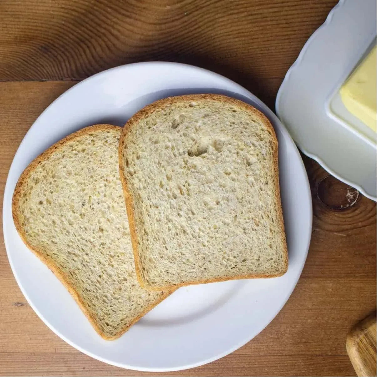 Two thin slices of golden-brown keto bread on a white plate, with butter in the background.
