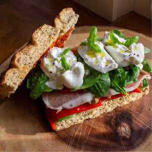 Open-faced focaccia sandwich with burrata, prosciutto, roasted red peppers, spinach, basil, and olive oil.