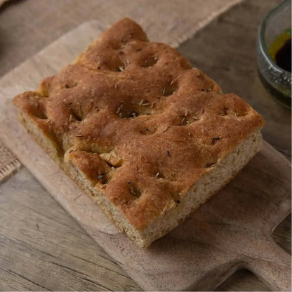 Golden brown keto focaccia bread with rosemary and sea salt on a rustic wooden board.